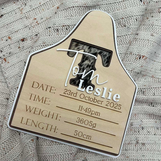 Wooden baby birth announcement plaque with engraved details on a textured fabric cowhide background