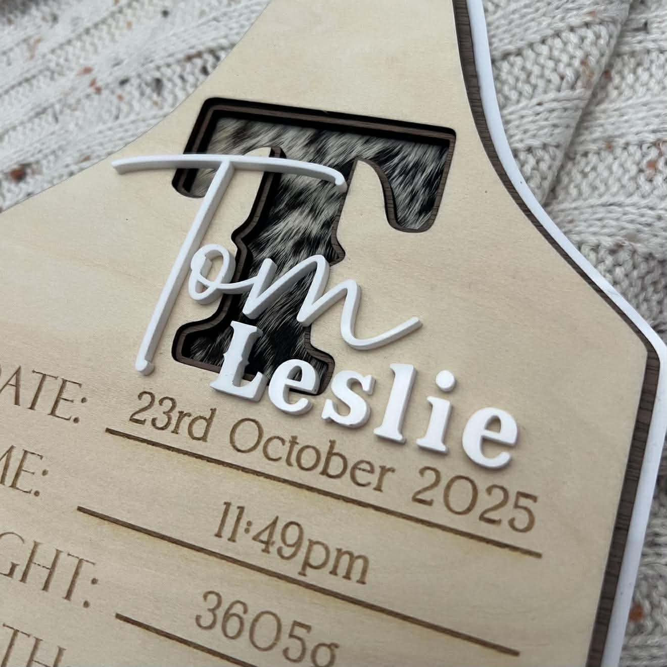 Wooden baby birth announcement plaque with engraved details on a textured fabric cowhide background