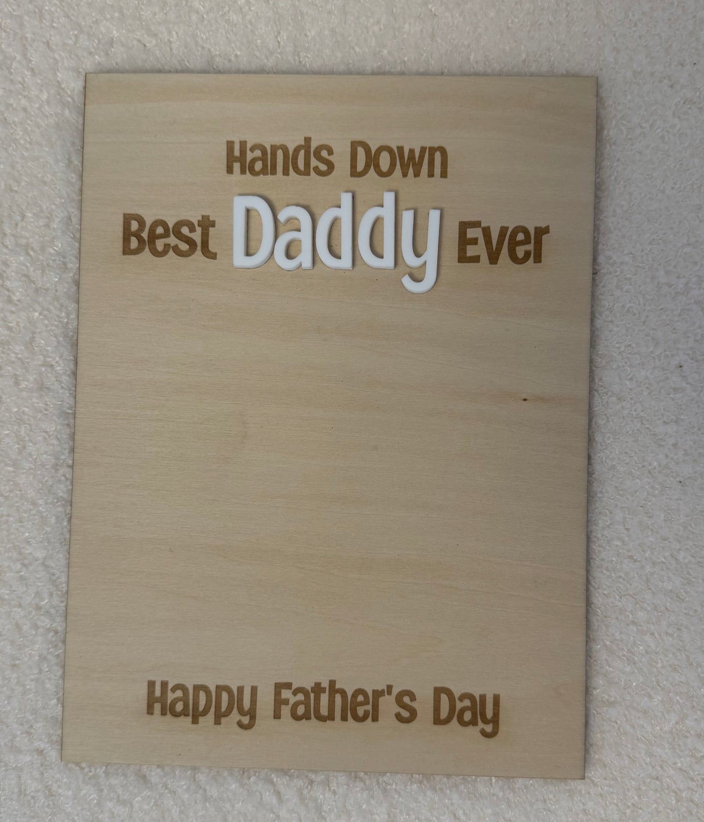 A rectangular wooden plaque engraved with 'Hands Down Best Daddy Ever' and 'Happy Father's Day' in brown lettering, displayed against a textured off-white wall.