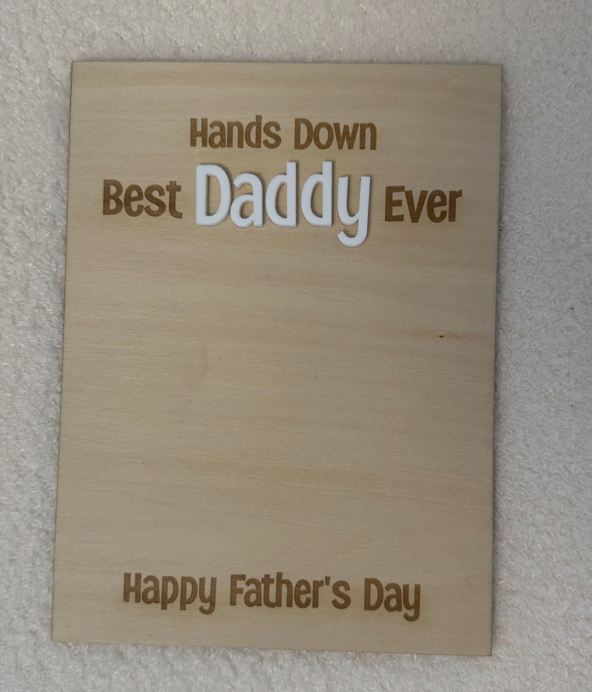 A rectangular wooden plaque engraved with 'Hands Down Best Daddy Ever' and 'Happy Father's Day' in brown lettering, displayed against a textured off-white wall.
