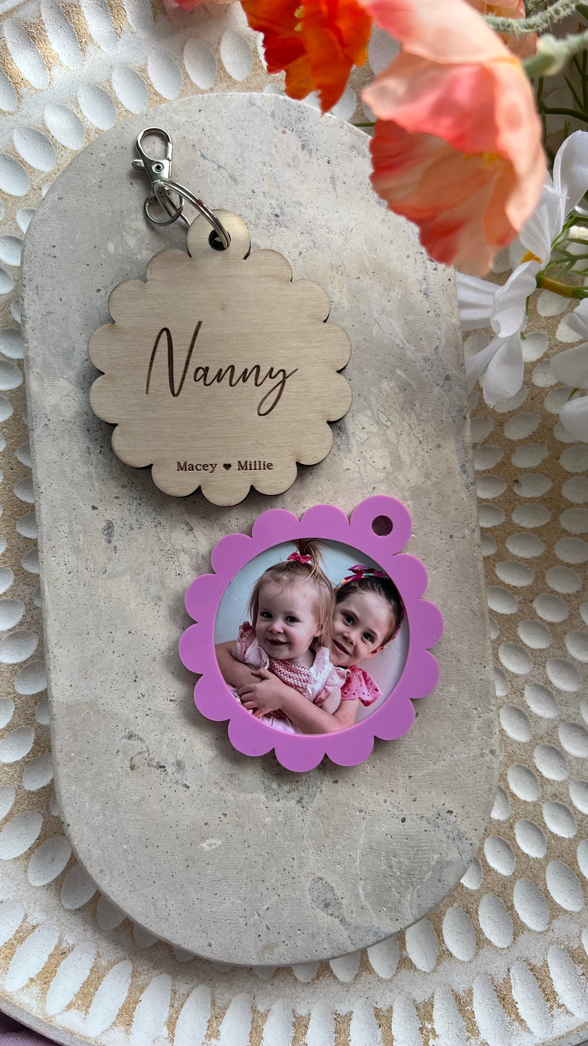 A personalized photo key ring with a scalloped edge design, featuring a custom photo of a baby and the name 'Nanny' printed on the reverse side, attached to a keyring.