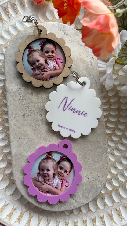 A personalized photo key ring with a scalloped edge design, featuring a custom photo and the a name printed on the reverse side, attached to a keyring