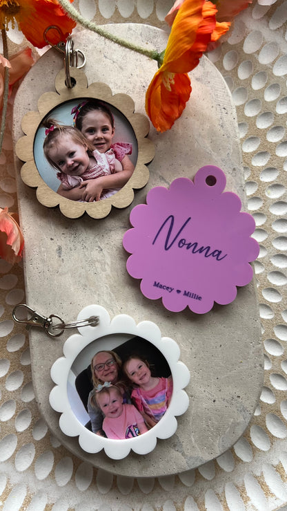 A personalized photo key ring with a scalloped edge design, featuring a custom photo and the a name printed on the reverse side, attached to a keyring